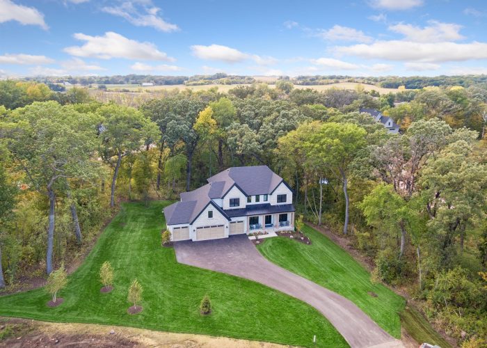Spacious modern home with lush green lawn and wooded surroundings.