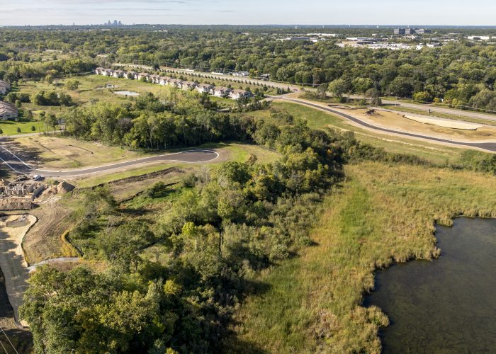 Aerial view of suburban road construction beside wooded wetlands