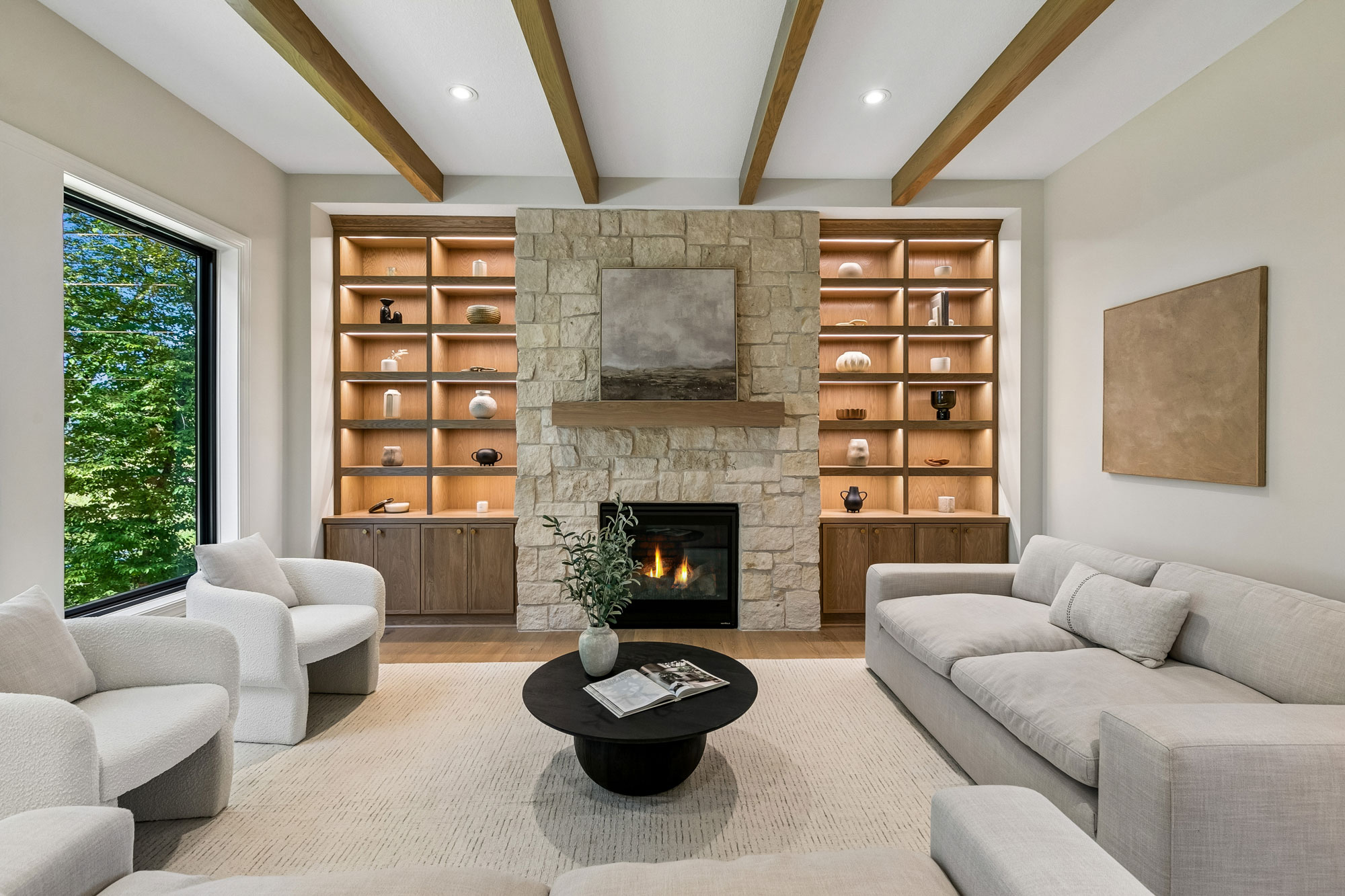Modern living room with a stone fireplace, built-in wood shelving, exposed ceiling beams, and neutral furnishings. 10380 Mallard Drive