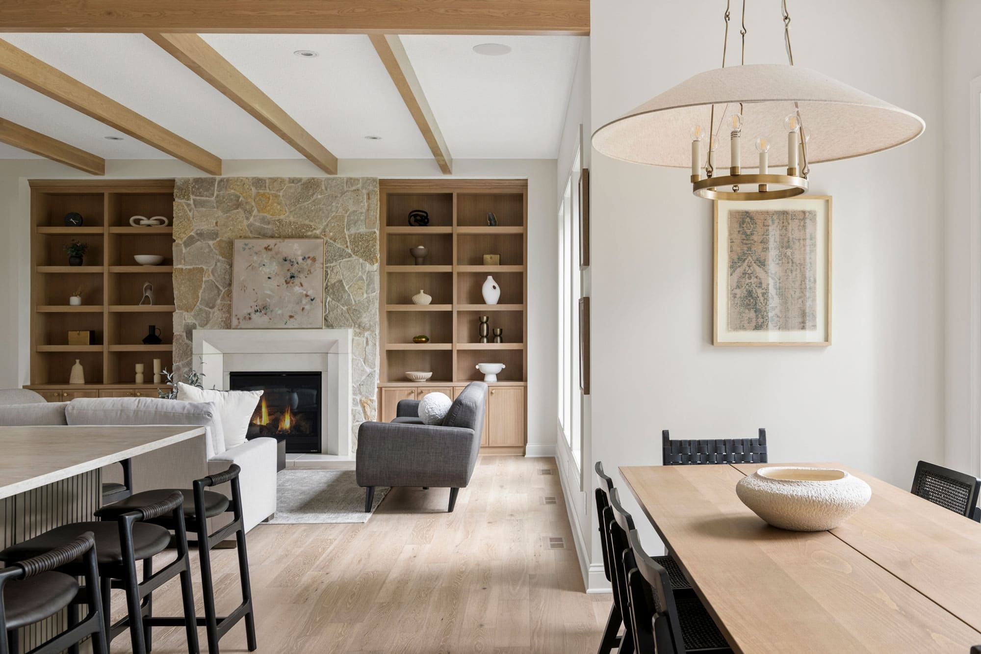 Modern living room with stone fireplace, built-in shelves, and wooden ceiling beams.