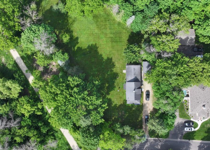 Aerial view of a lush green backyard with trees and a small house in a residential neighborhood.